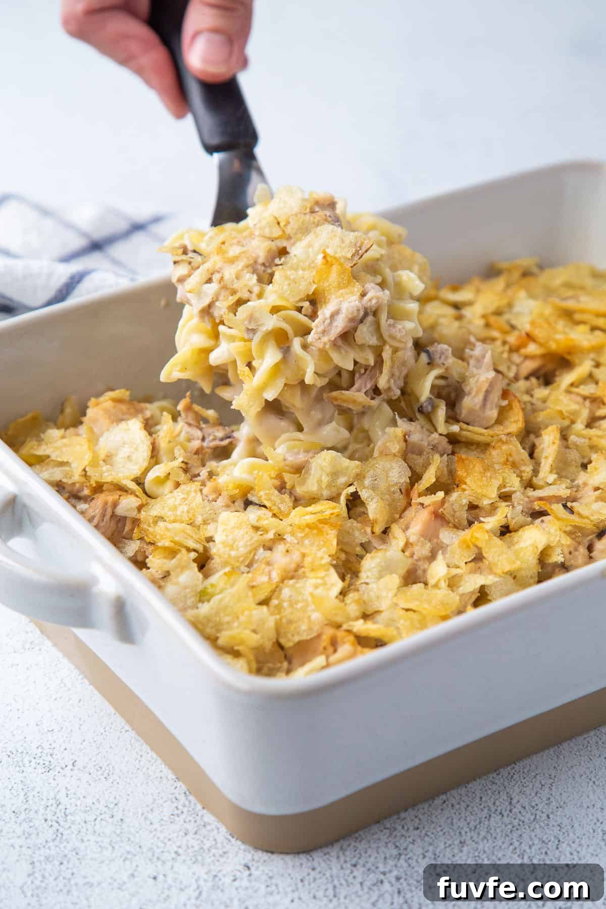 hand lifting a scoop of tuna noodle casserole out of a casserole dish.