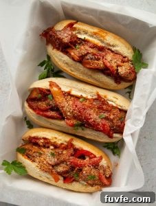 overhead shot of 3 sausage pepper sandwiches in large baking dish garnished with fresh parsley