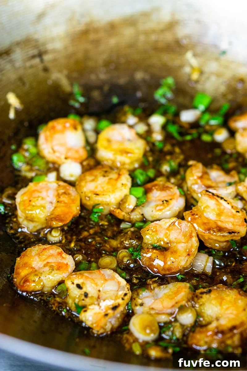 Shrimp being sauteed in a skillet with a ginger garlic sauce.