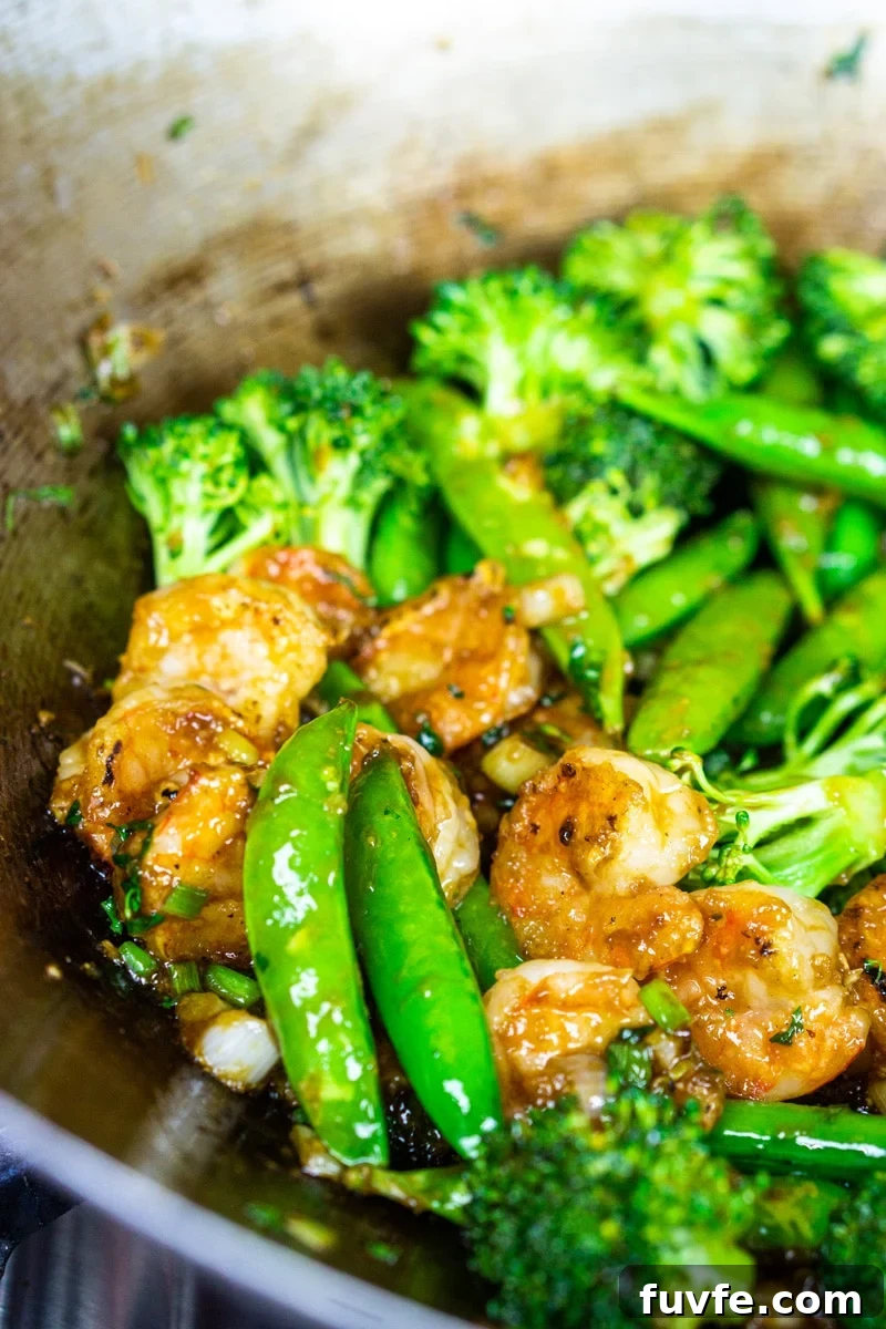 Shrimp stir fry in a skillet with broccoli and sugar snap peas.
