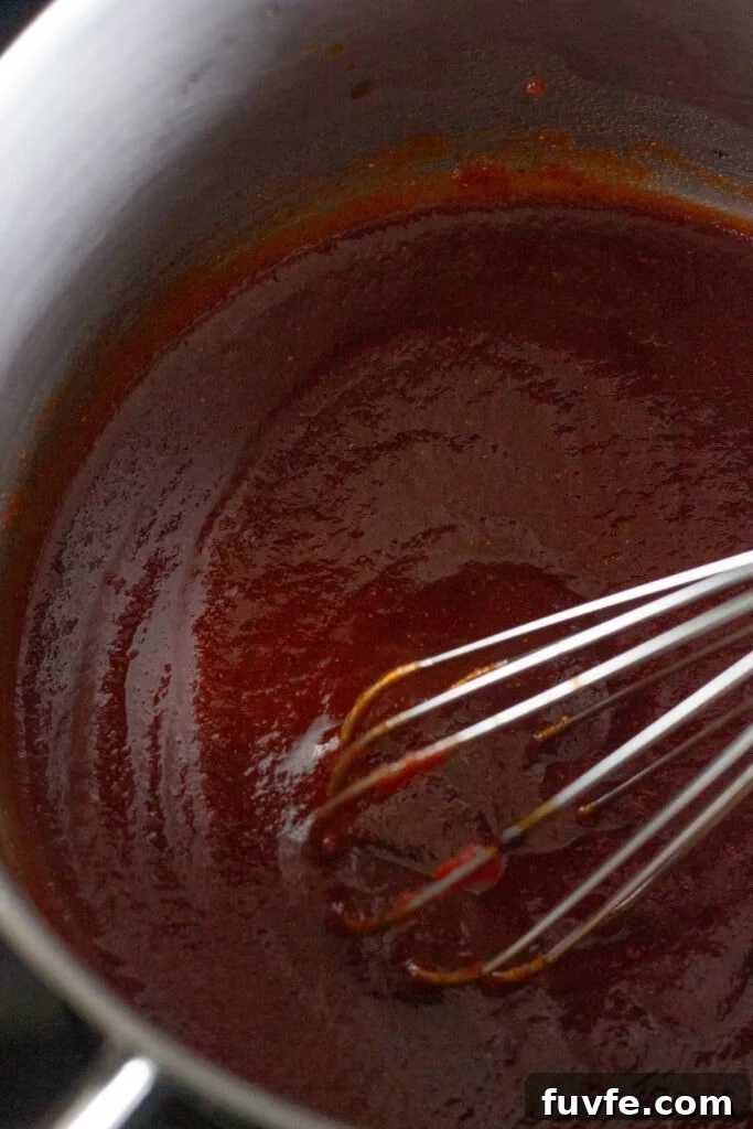 Close up of a whisk stirring bbq sauce in a small sauce pan.