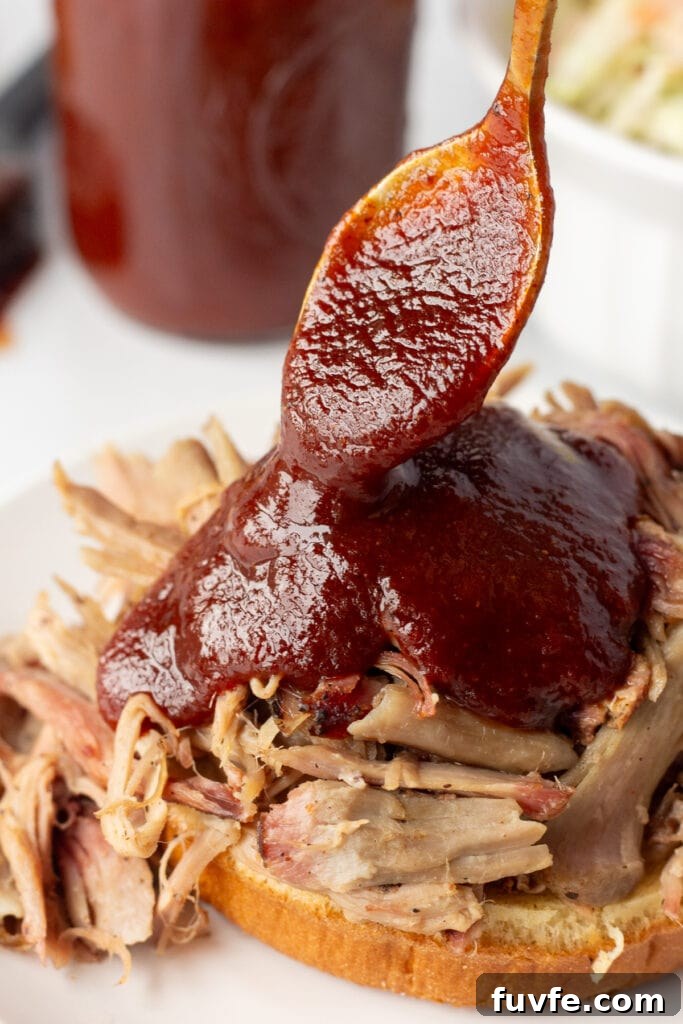 Close up of maple bbq sauce being spooned onto a pulled pork sandwich.