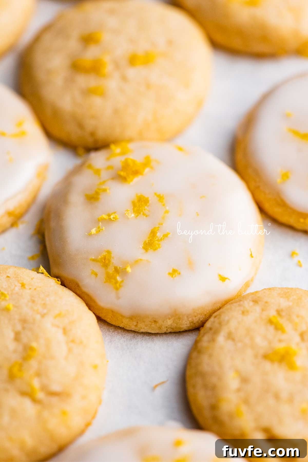 Lemon iced and plain lemon shortbread cookies garnished with lemon zest on white parchment paper.