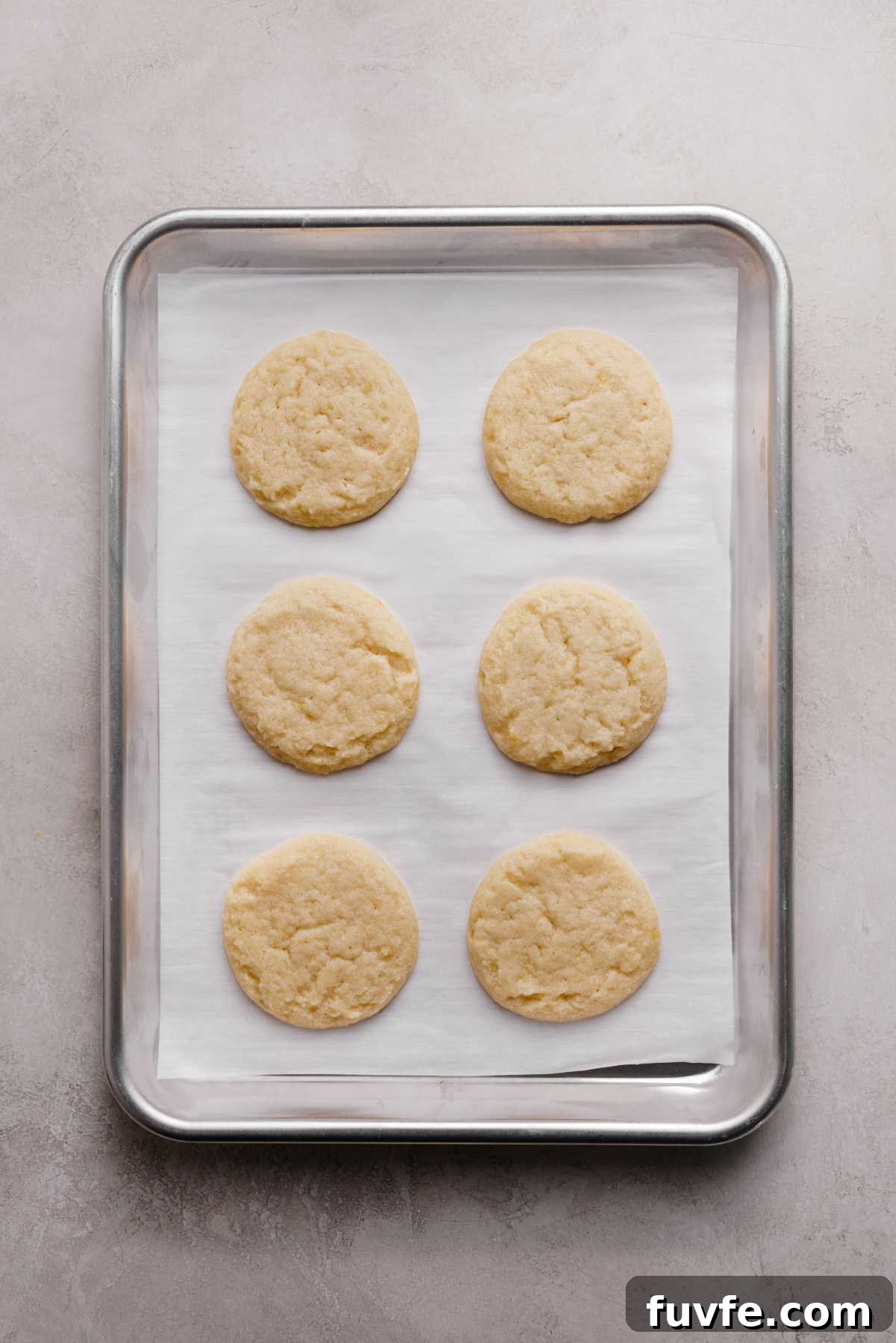 Just baked lemon shortbread cookies on a white parchment paper lined baking sheet on a grey marbled background.