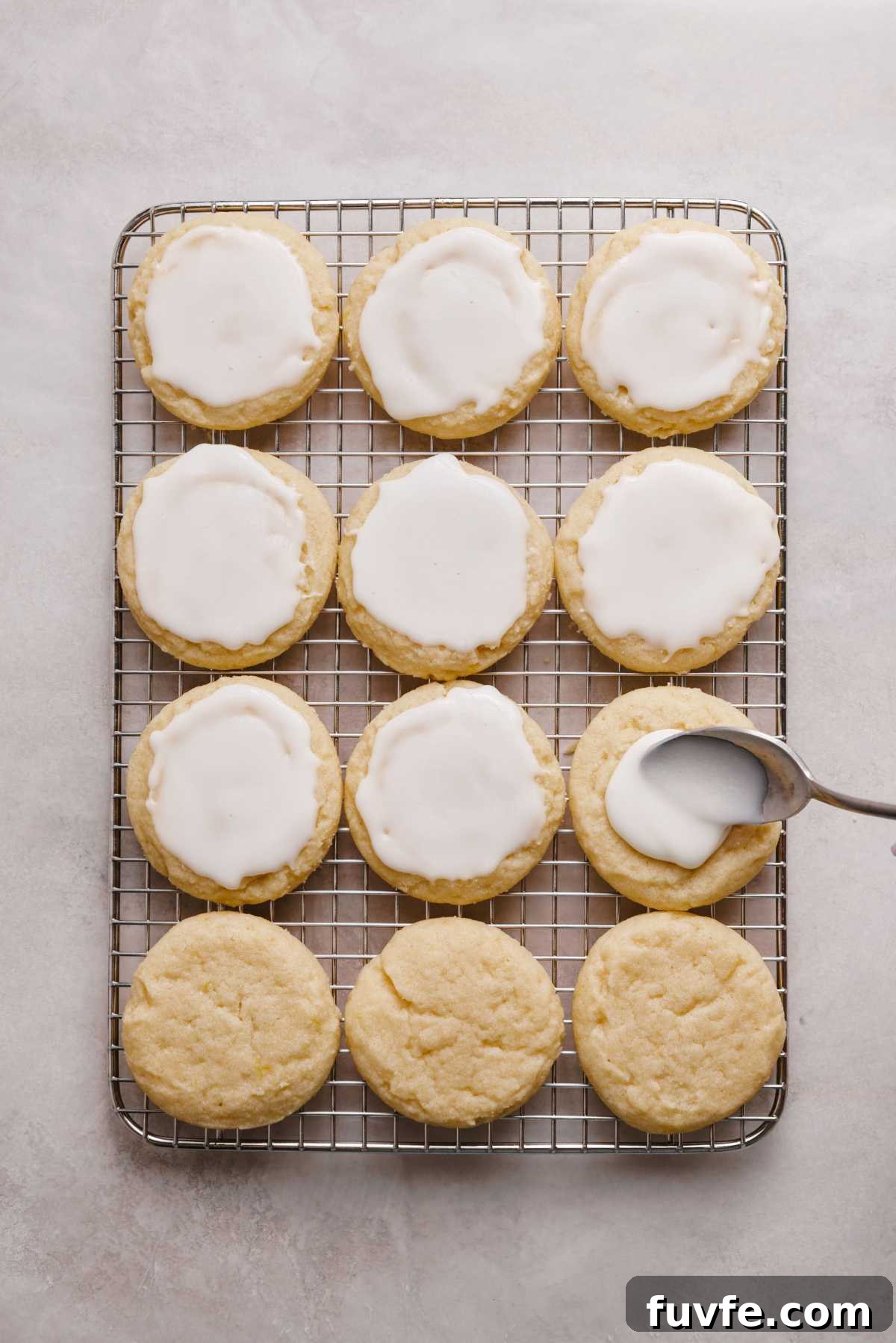 Topping lemon shortbread cookies on a wire cooling rack with lemon glaze using a spoon.