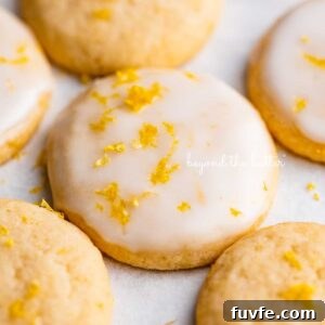 Lemon iced and plain lemon shortbread cookies garnished with lemon zest on white parchment paper.