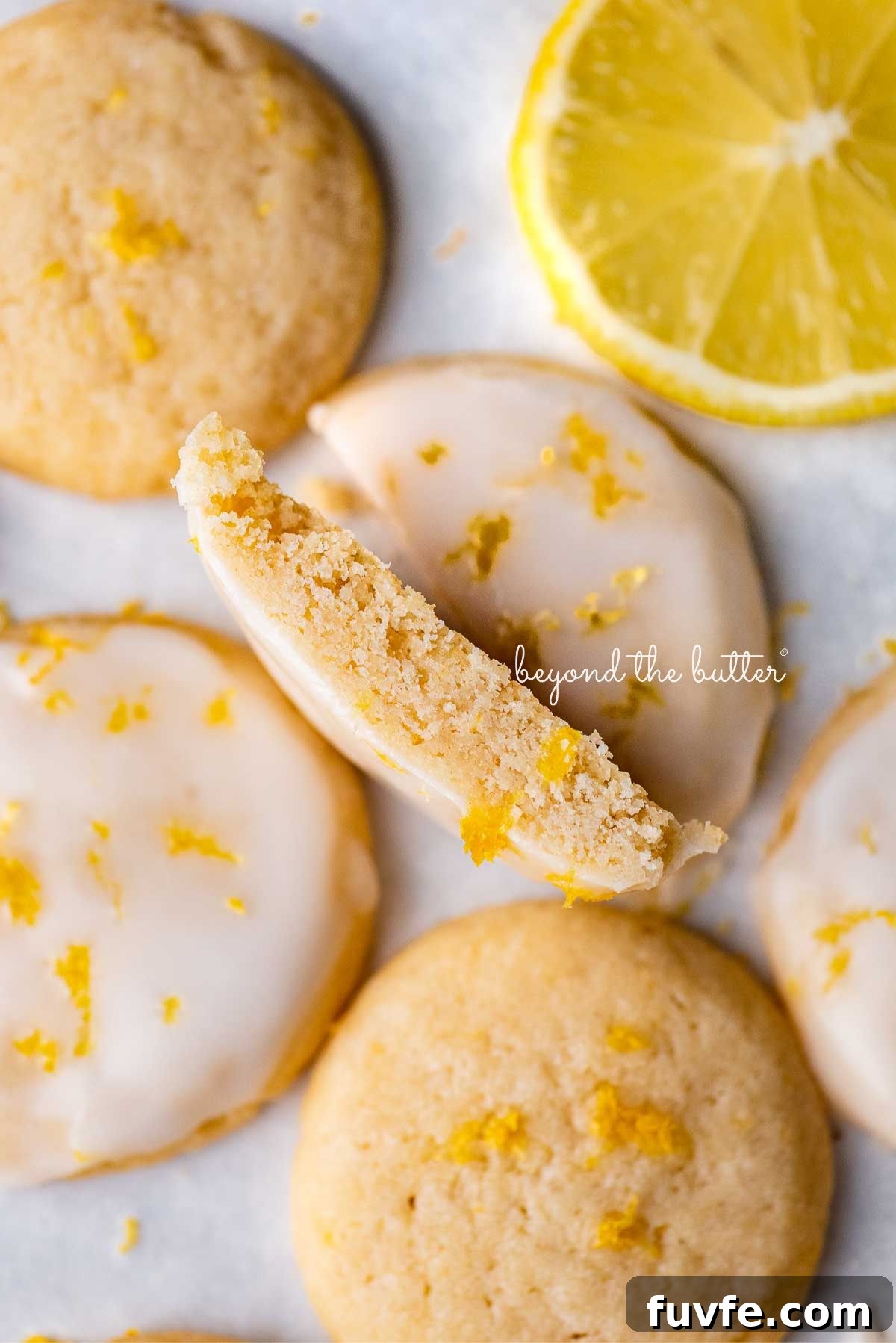 Lemon shortbread cookies with center cookie cut in half with sliced lemon on white background.