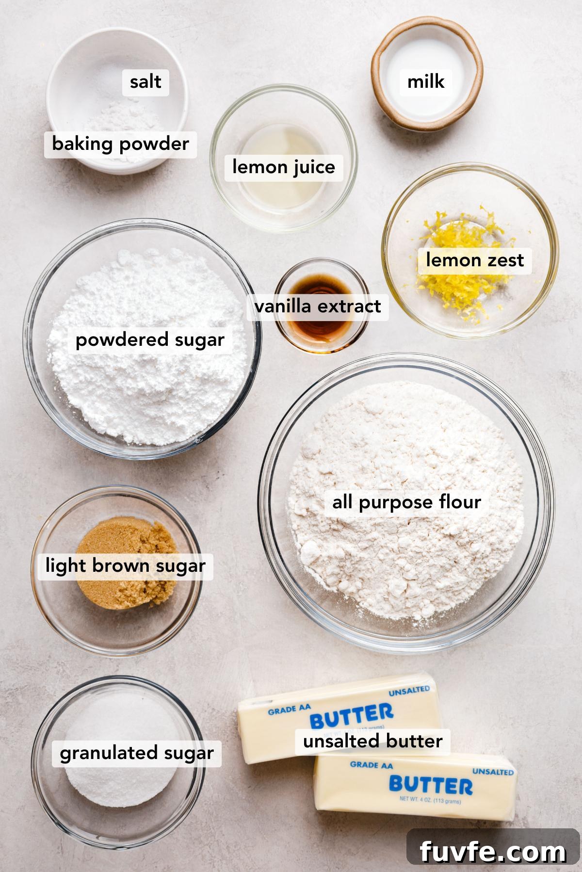 Ingredients in various size bowls labeled as salt, baking powder, milk, powdered sugar, vanilla extract, lemon juice, lemon zest, light brown sugar, all purpose flour, granulated sugar, and unsalted butter on a white marbled background.