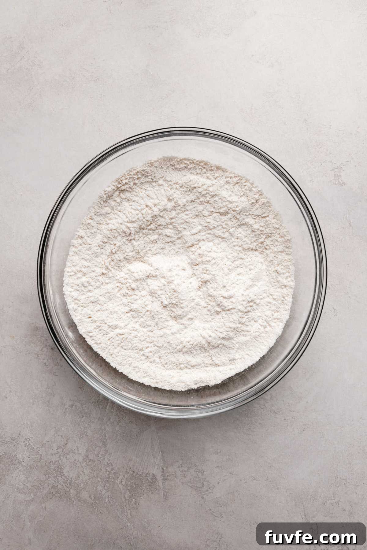 Whisked all purpose flour, baking powder, and salt in a large glass mixing bowl on a grey marbled background.