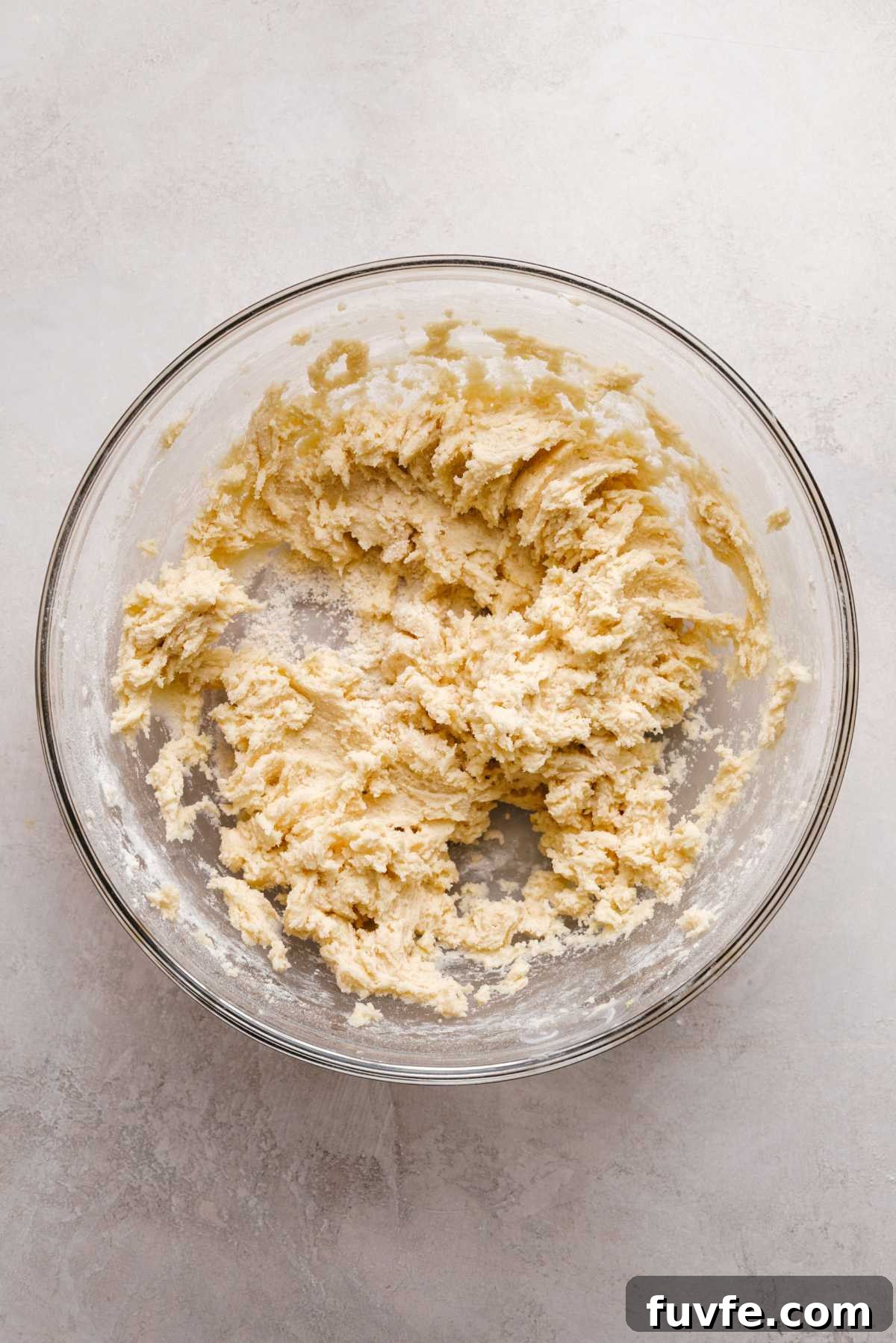 Wet and dry lemon shortbread cookie ingredients mixed together in a large glass bowl on a grey marbled background.