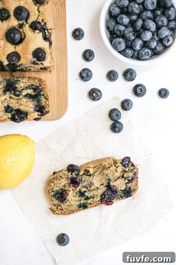 Lemon Blueberry Quick Bread Recipe for Moist Zesty Loaves 7 Healthy lemon blueberry bread with lemon and a bowl of blueberries sitting nearby. A piece of blueberry bread is sitting on parchment.