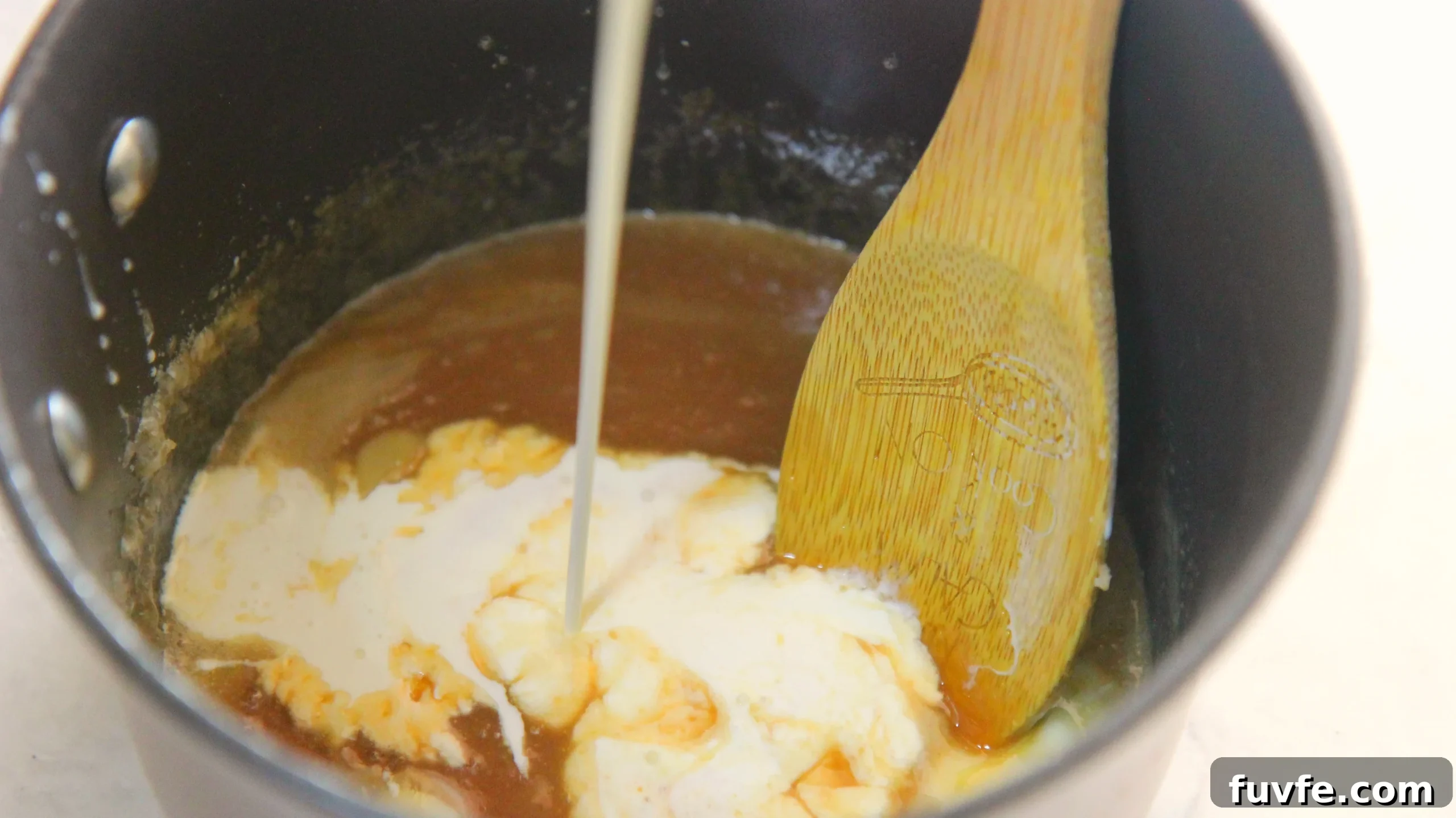 caramel sauce and heavy cream in a sauce pan with a wooden spoon