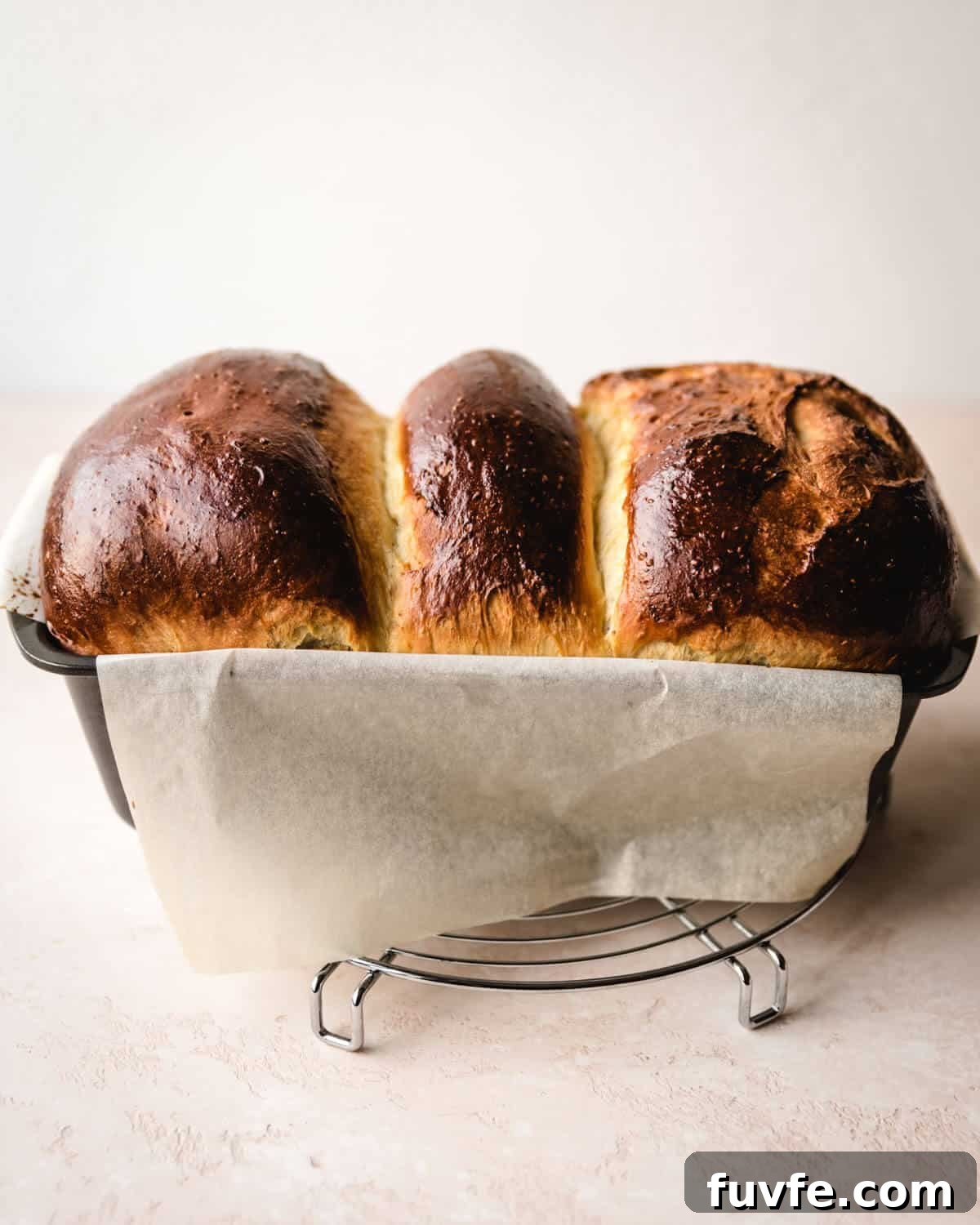 Creamy Condensed Milk Bread Recipe for Soft Homemade Loaf 33 Baked condensed milk bread sitting on parchment paper in a loaf pan on top of a cooling rack.