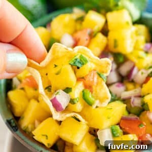 A hand holding up a chip with pineapple salsa on it over the bowl.
