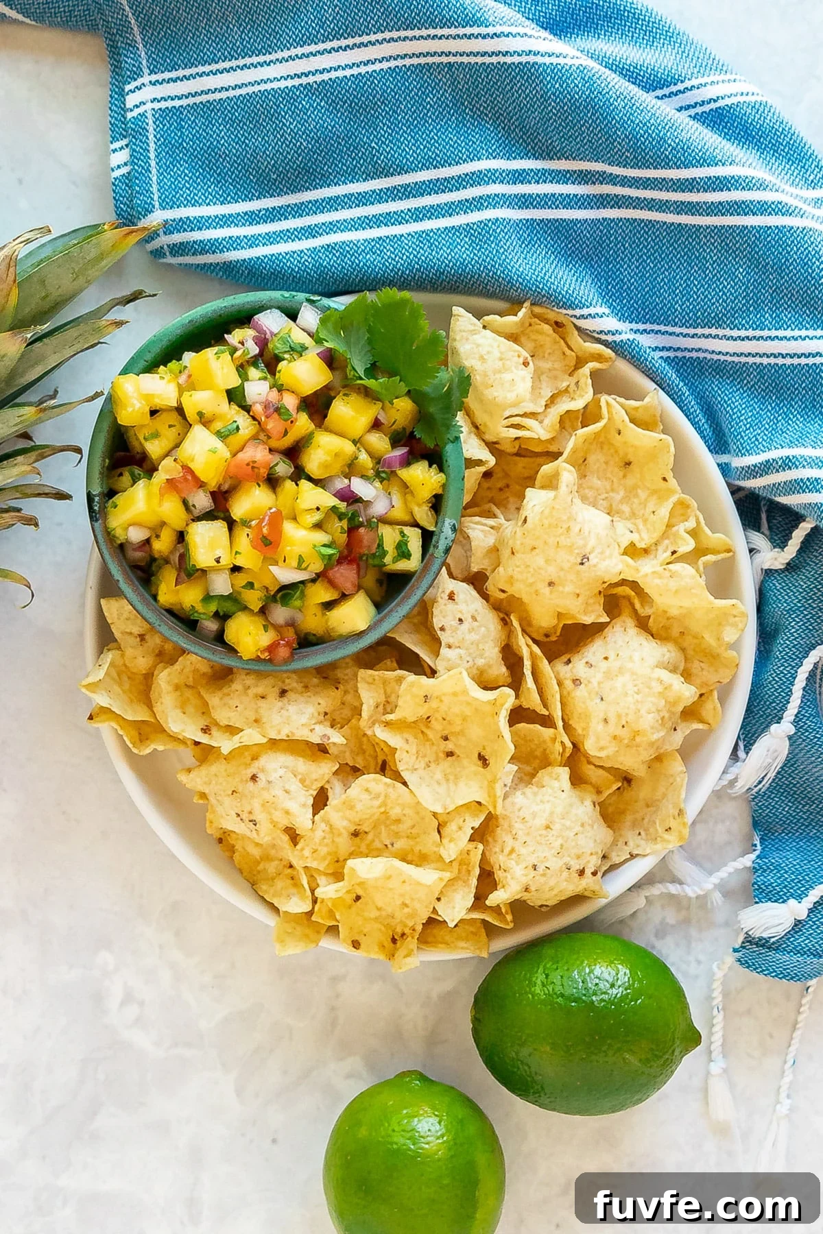 An overhead image of pineapple salsa and chips with a blue towel.