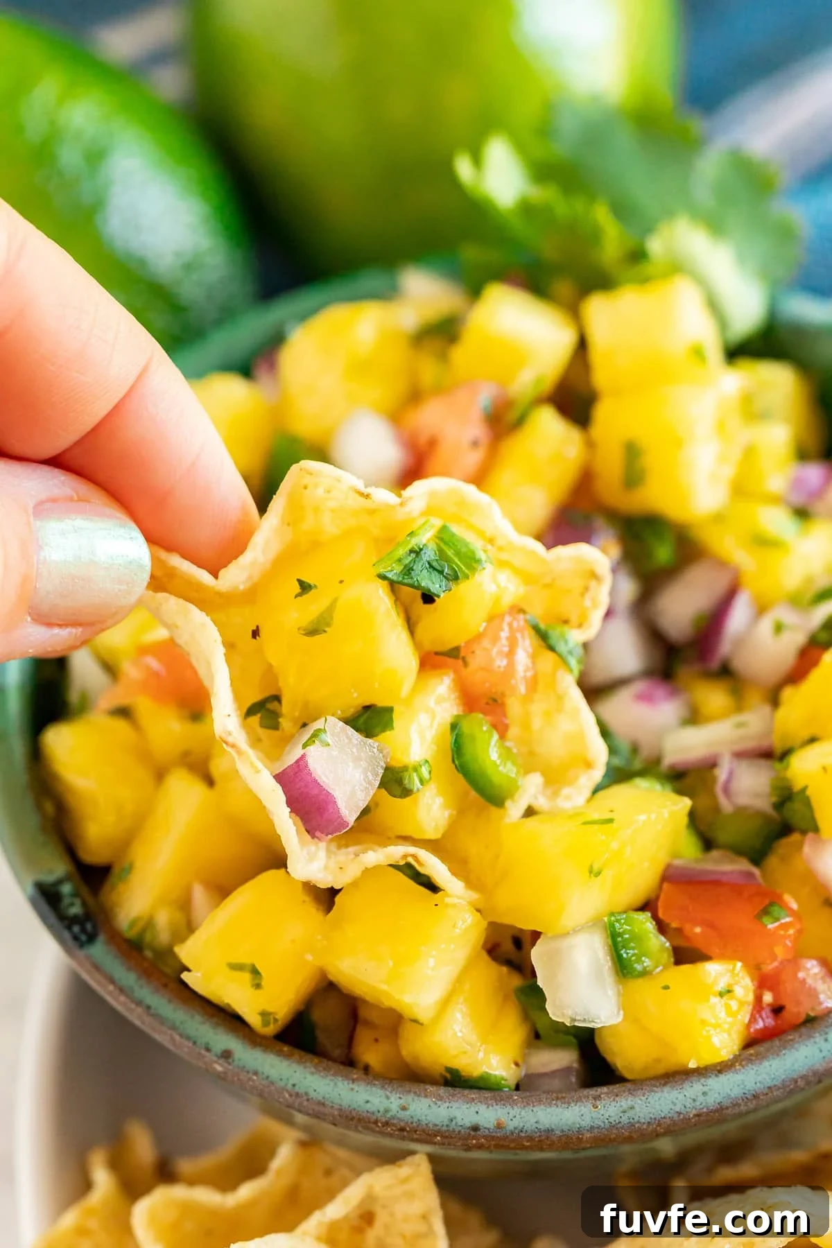 A hand holding up a chip with pineapple salsa on it over the bowl.