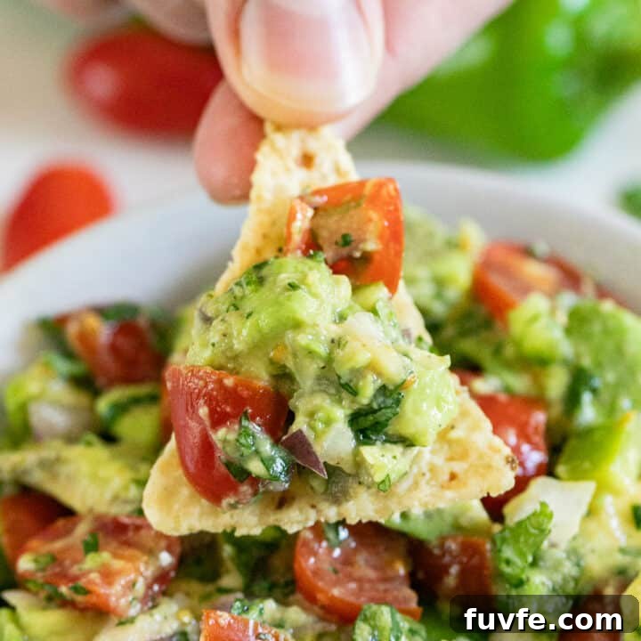 A hand holding a chip with avocado salsa.
