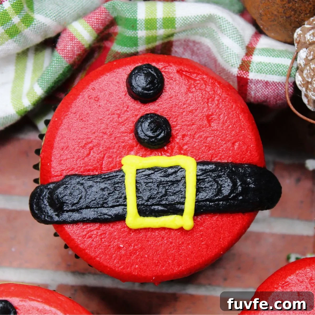 A close-up of a single cupcake that is made with gluten and dairy free ingredients and decorated to look like Santas Billy with his belt and coat buttons.