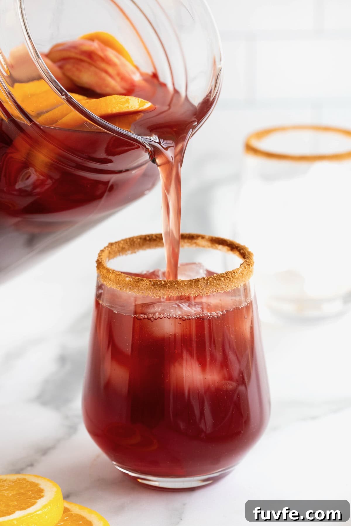 Apple ciders sangria being poured from a pitcher into a cinnamon sugar rimmed glass with ice.