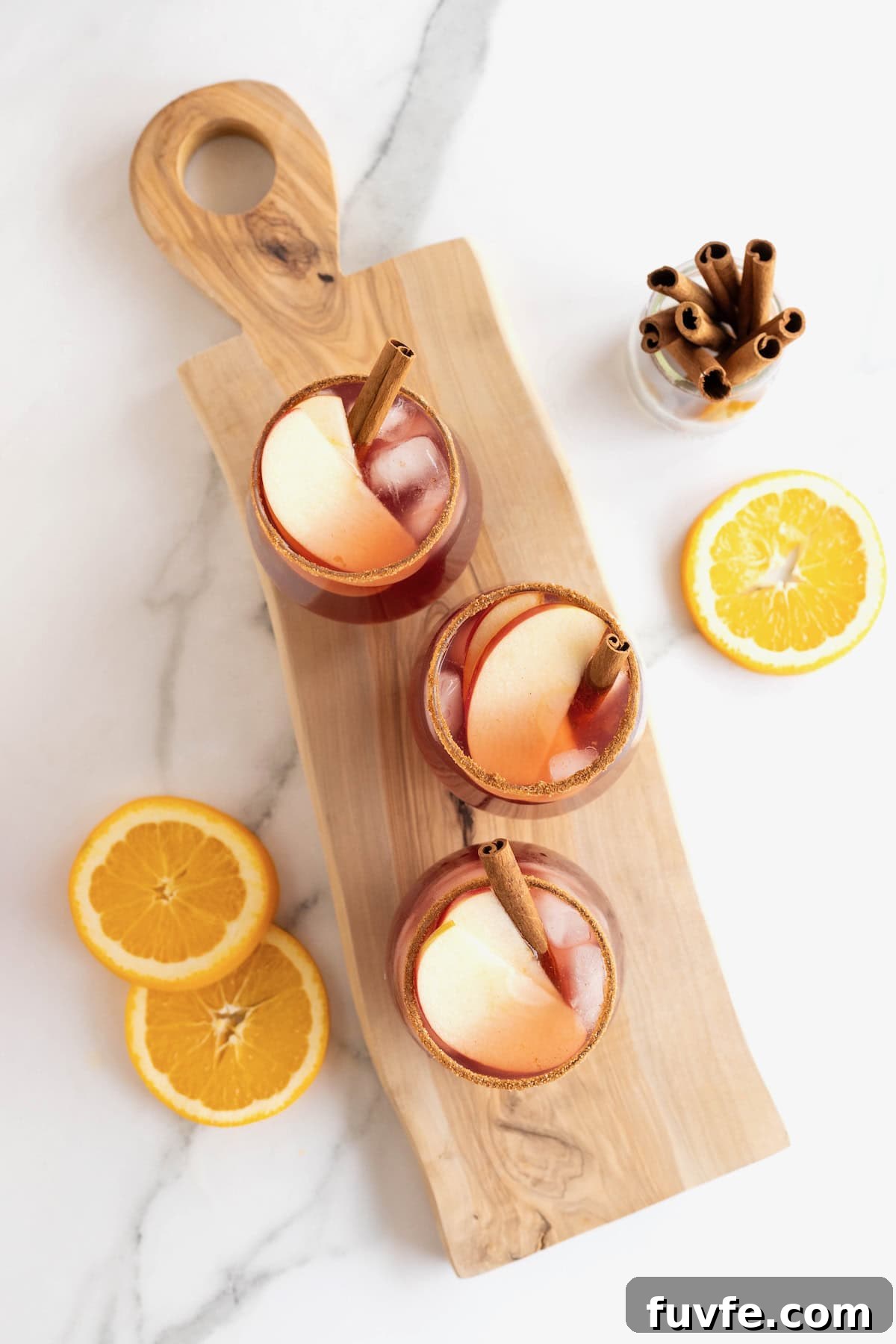 Three glasses of apple cider sangria on a long rectangular wooden cutting board.
