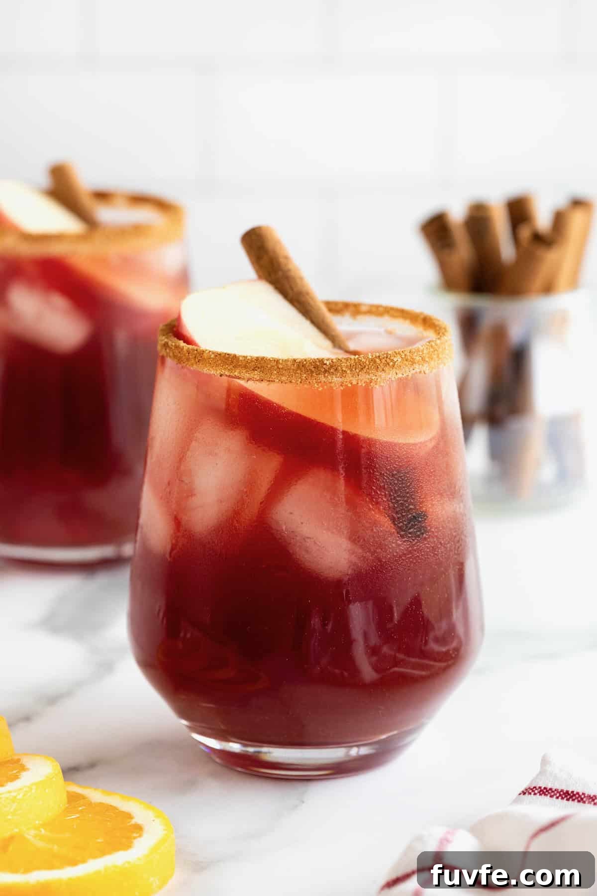 Two glasses of apple cider sangria in cinnamon sugar rimmed glasses on a white marble counter.