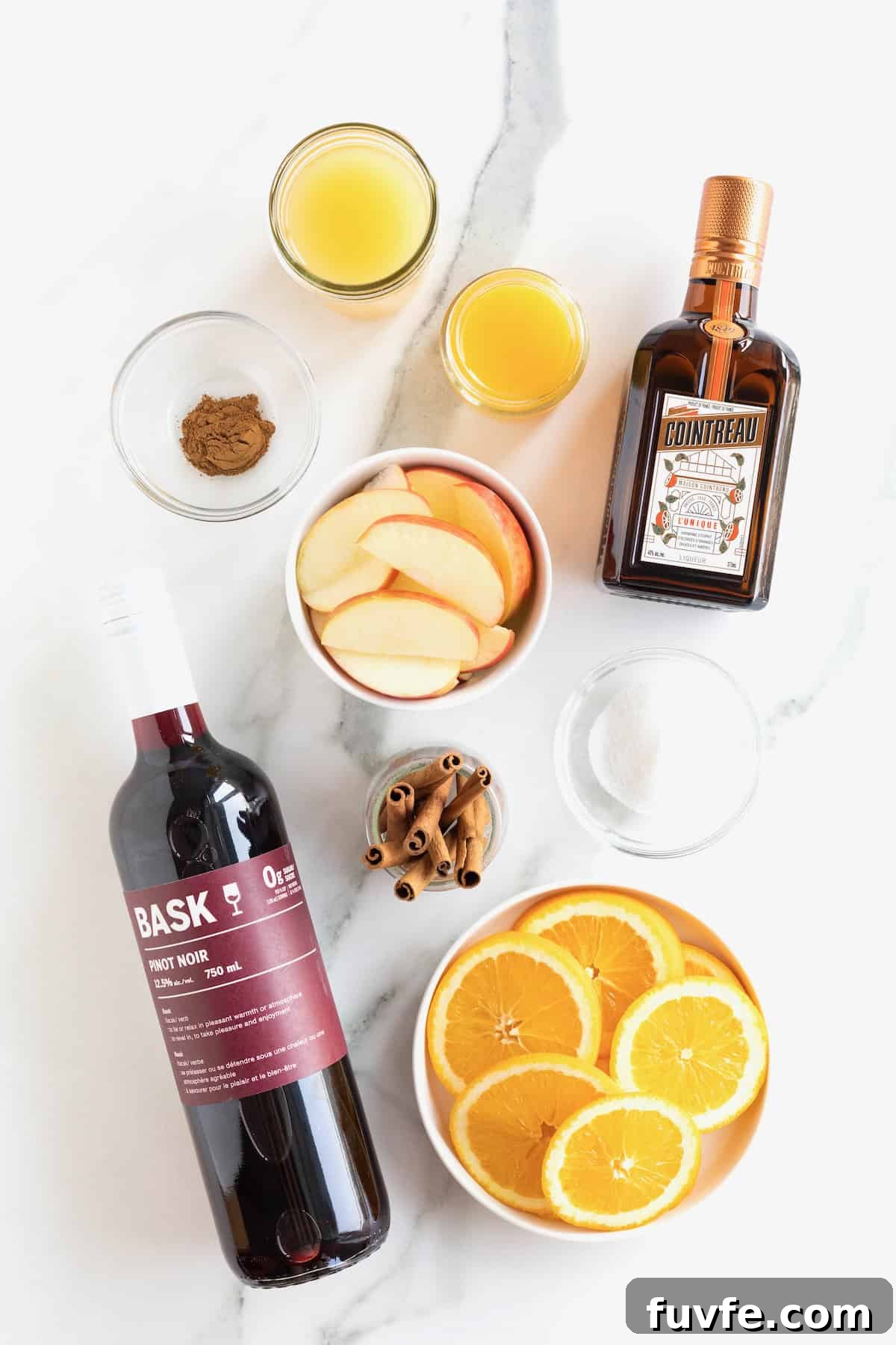 Ingredients to make apple cider sangria on a white marble counter.