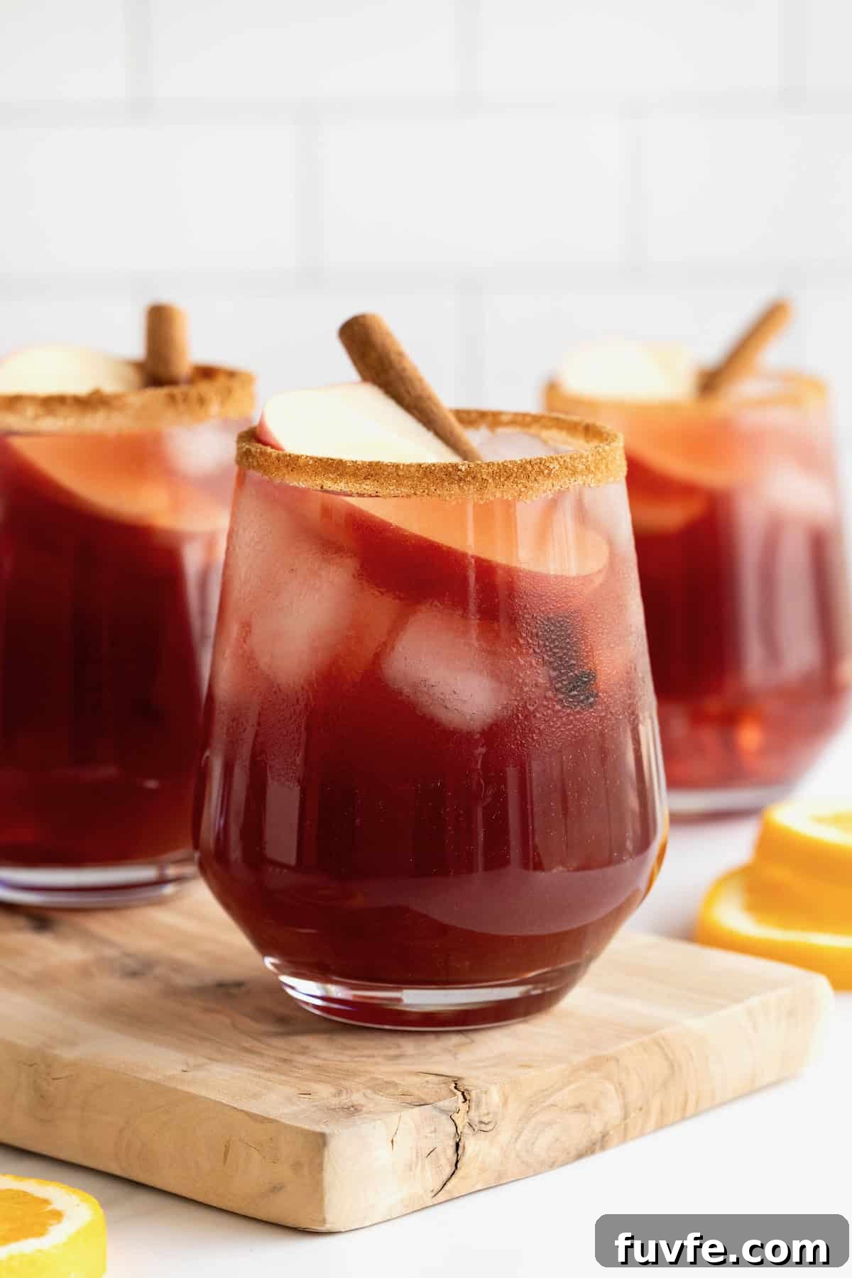 Three glasses of apple cider sangria on a long rectangular wooden cutting board.
