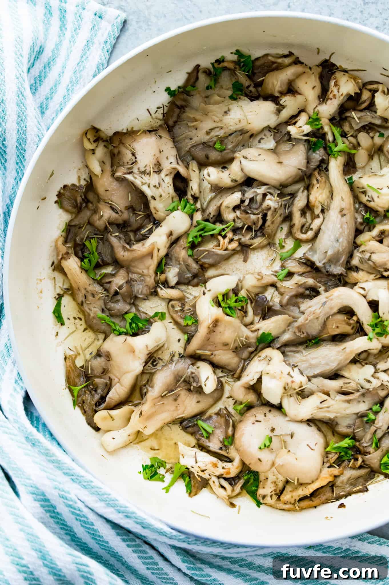 Crispy Pan-Fried Oyster Mushrooms with Garlic Butter 2 A pan filled with fried oyster mushrooms topped with fresh herbs.
