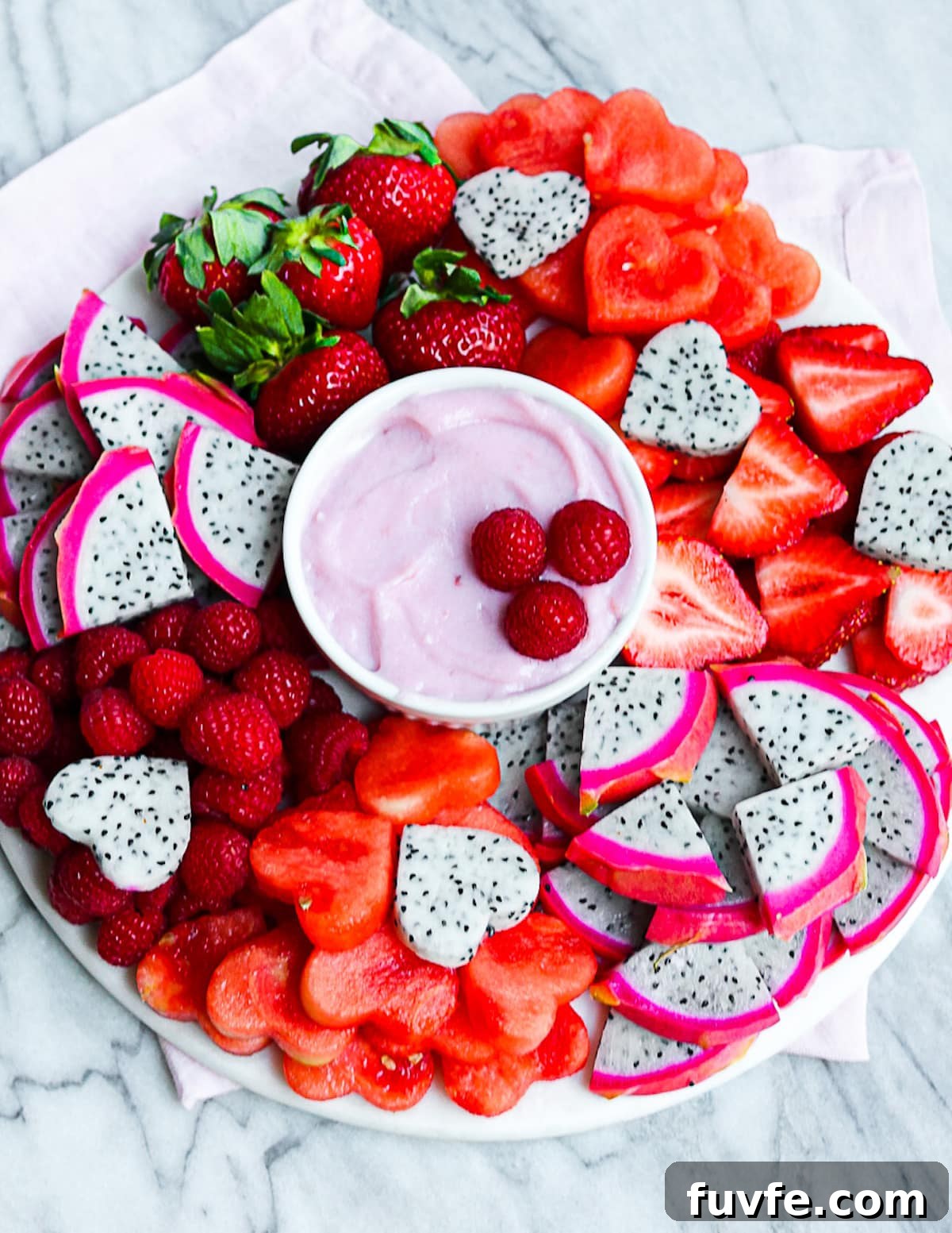 A platter filled with fresh red fruits and with a bowl of dip in the middle