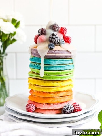 A stack of colorful pancakes with frozen fruit on top and a drizzle of white sugar sauce on top.