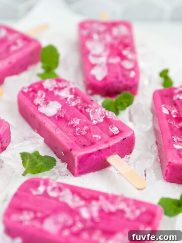 6 popsicles on a white marble slab. The pops and board are garnished with sprigs of fresh green mint and crushed ice.