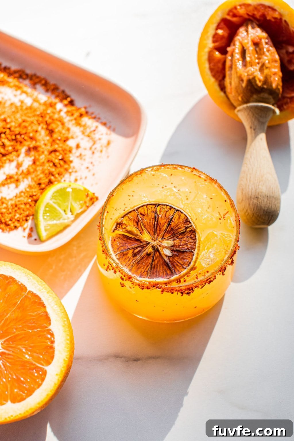 orange margarita with a slice of orange in it and tajin around the rim 