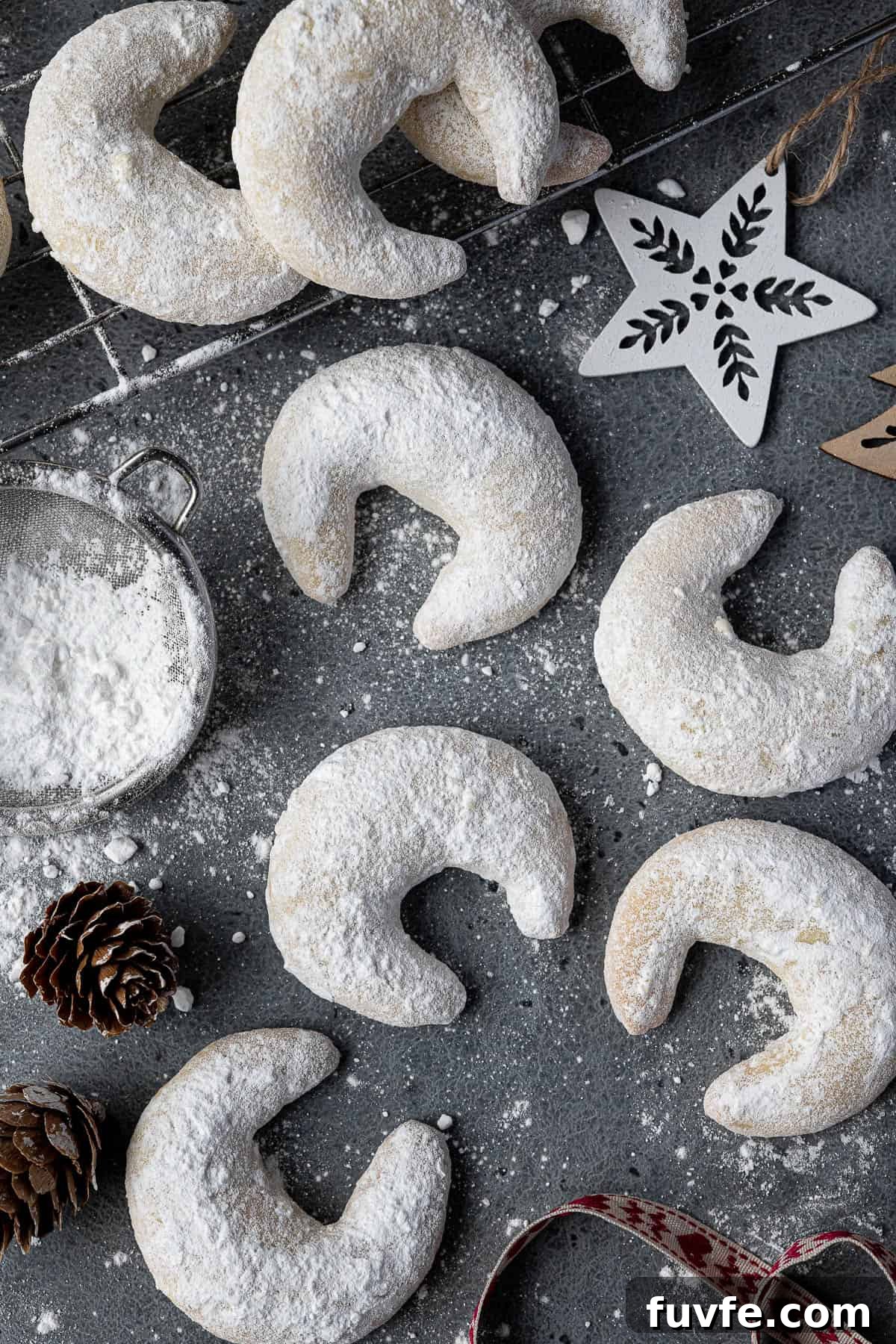 Vegan vanillekipferl on a grey surface with pine cones and Christmas ornaments.