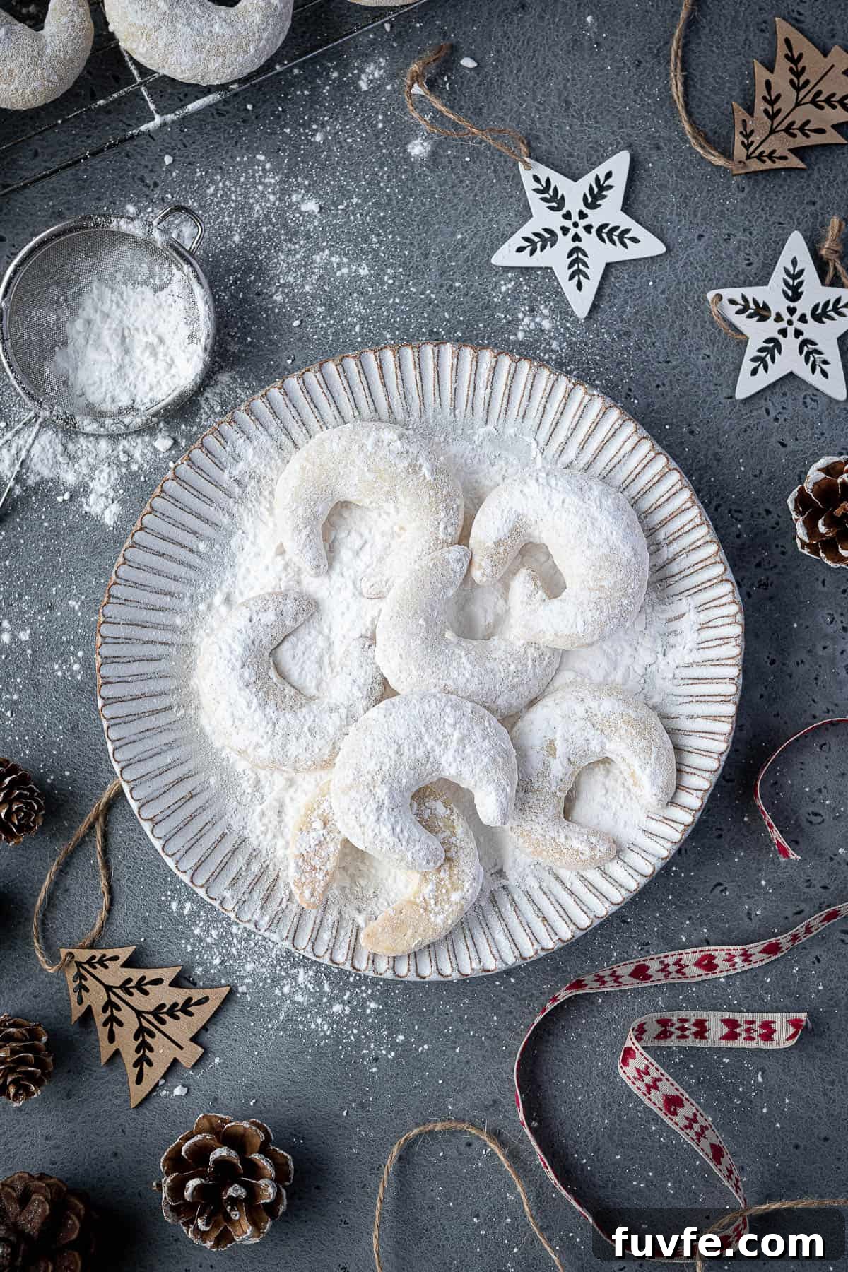 Vegan vanillekipferl on a white plate surrounded by Christmas ornaments.
