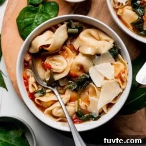 A bowl with tortellini and wilted spinach in a tomato broth garnished with parmesan cheese.