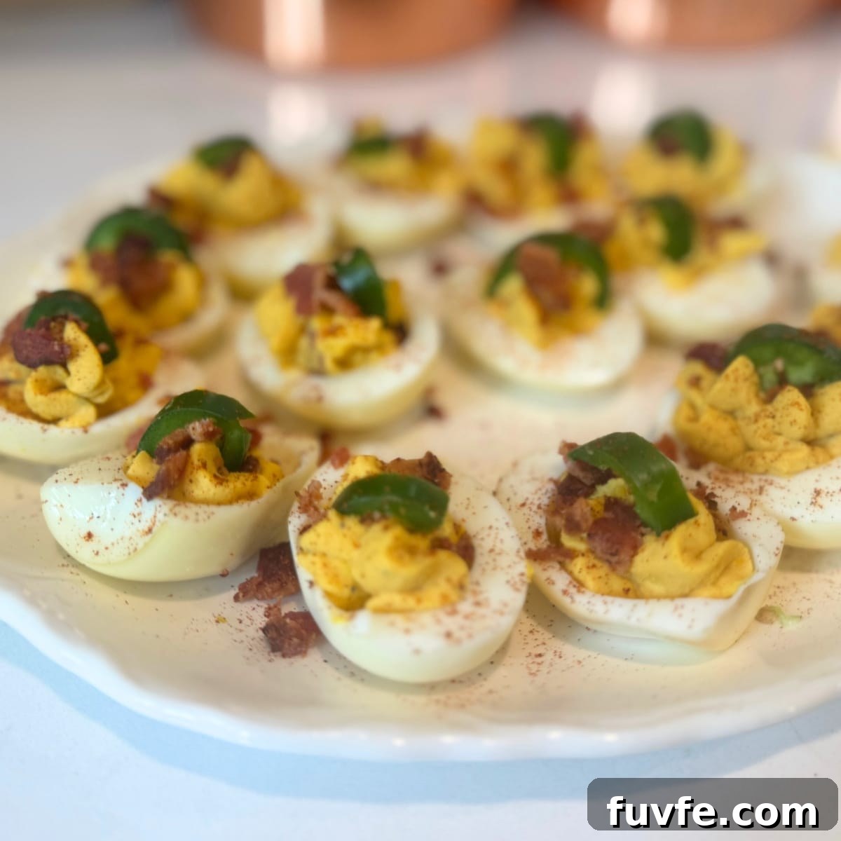 A platter of Bacon Jalapeño Deviled Eggs garnished with crispy bacon crumbles, fresh jalapeño rounds, and a dusting of smoked paprika.