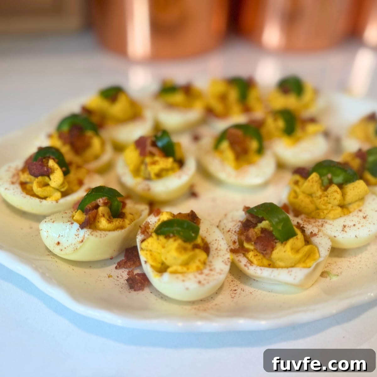 Close-up of farmhouse-style deviled eggs topped with bacon and jalapeños on a serving plate.