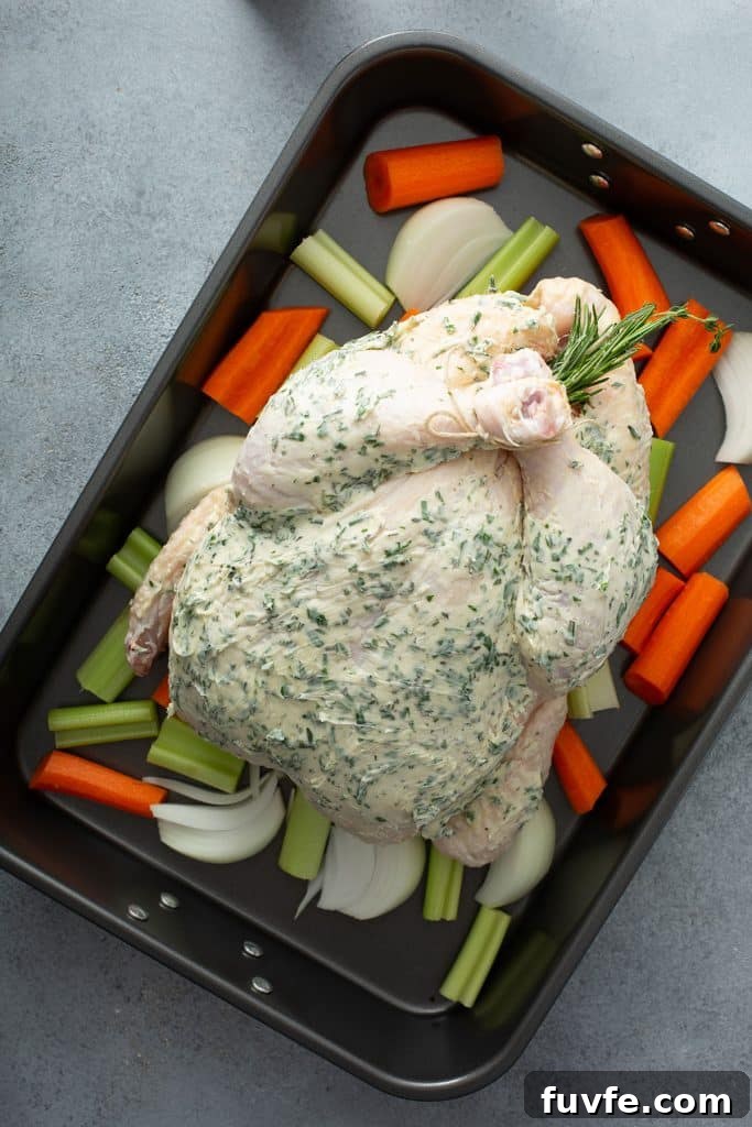 Herb-Butter Roast Chicken Recipe for Juicy Crispy Skin 7 A whole chicken slathered with herb butter in a roasting pan over vegetables.