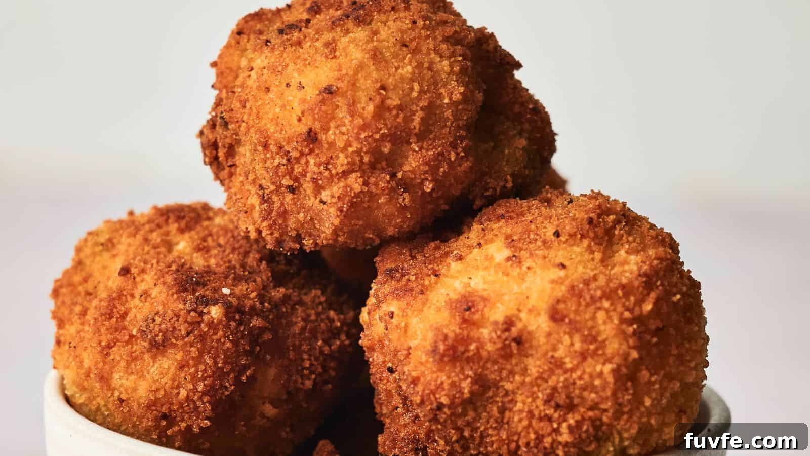 A bowl of golden-brown, crispy fried arancini served in a white dish on a plain background.
