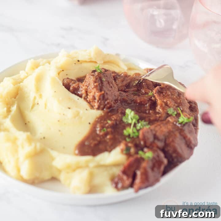 A square photo with a white plate with mashed potatoes and stew with gingerbread and apple syrup on top. A white marble surface. A fork pierces the meat.