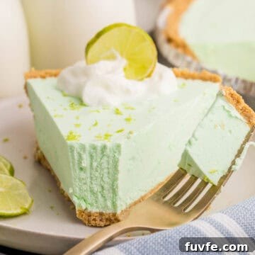 No-Bake Key Lime Jello Pie with Cool Whip Topping 11 Close-up of a slice of key lime Jello pie with a bite on a fork beside it. The pie is topped with whipped cream, lime zest, and a lime slice, showing its airy and creamy whipped texture.