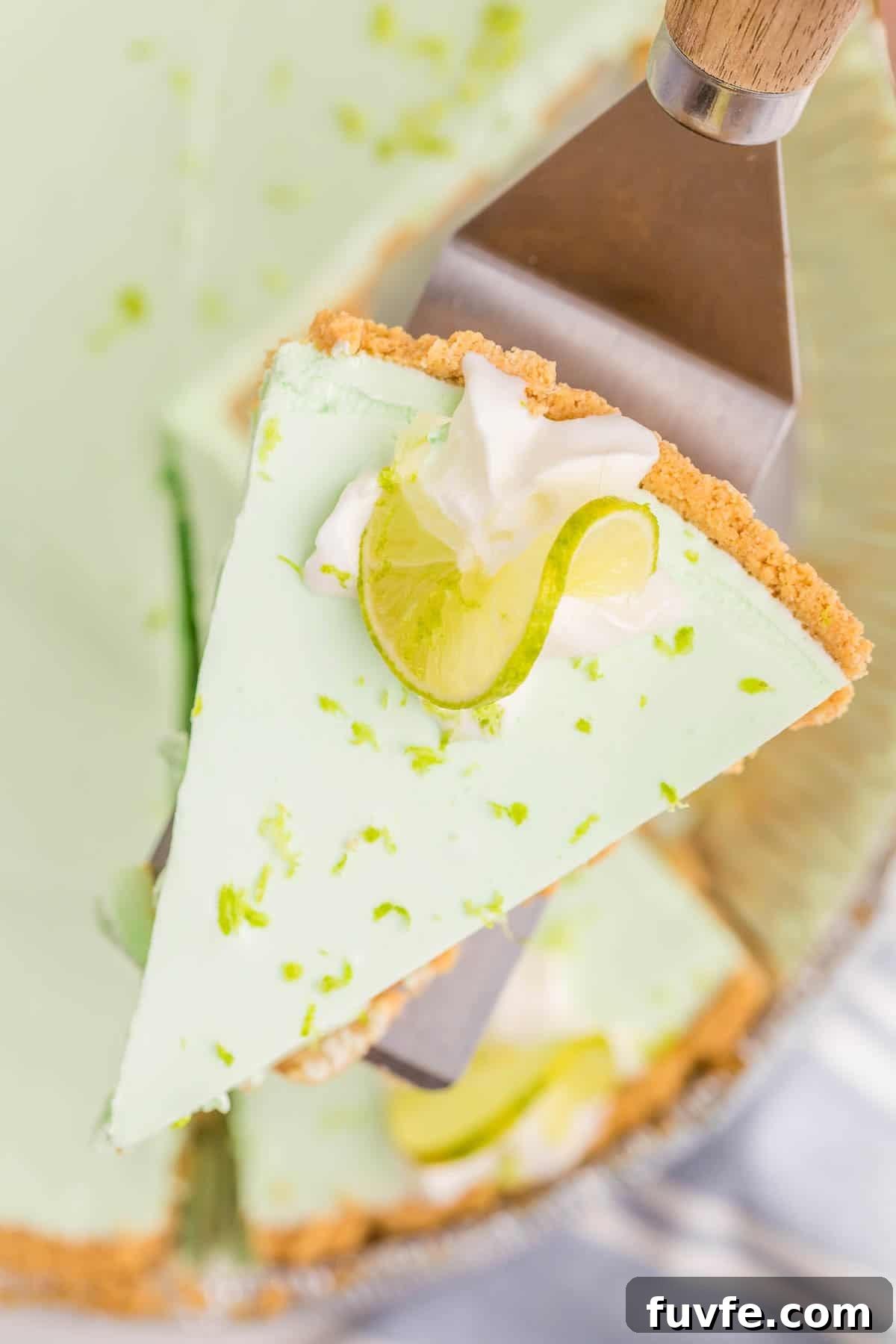 No-Bake Key Lime Jello Pie with Cool Whip Topping 8 Slice of key lime Jello pie being lifted from the pie with a server. Whipped cream, a lime slice, and lime zest decorate the top, showing the pie’s smooth and creamy texture.
