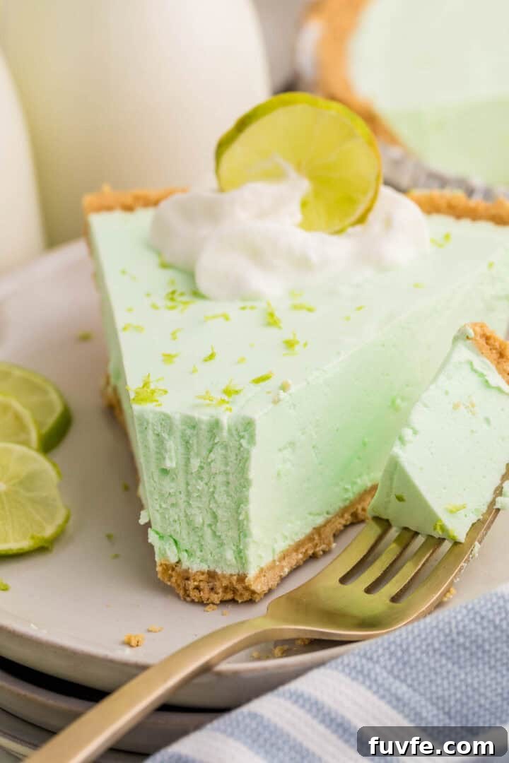 No-Bake Key Lime Jello Pie with Cool Whip Topping 9 Slice of key lime Jello pie with a bite-sized piece resting on a fork in the foreground. Whipped cream, lime zest, and a lime slice top the pie, highlighting its thick and creamy filling.
