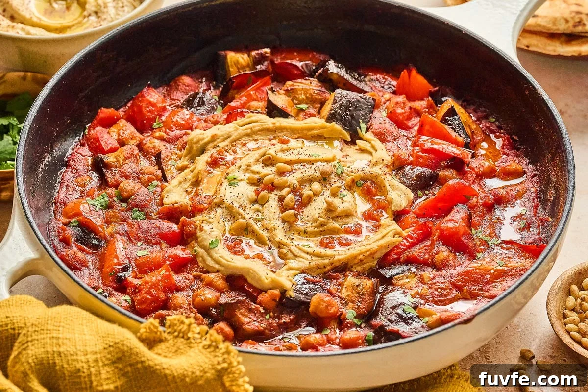 One-Pan Mediterranean Chickpea Skillet with Tomatoes & Spinach 2 Enjoy a Mediterranean chickpea skillet featuring roasted eggplant, red peppers, and chickpeas, all topped with creamy hummus, fresh herbs, and crunchy pine nuts for a delightful harmony of flavors.