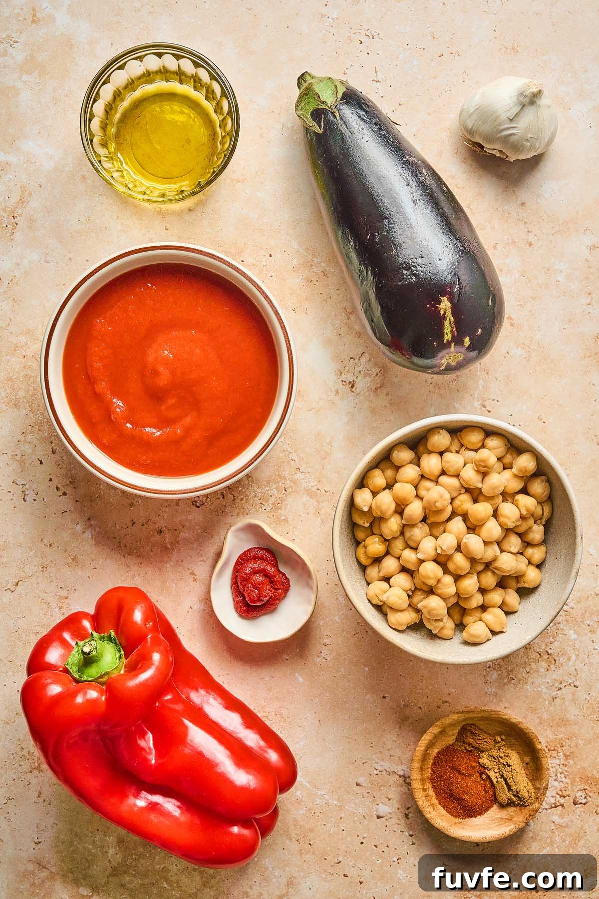 One-Pan Mediterranean Chickpea Skillet with Tomatoes & Spinach 14 A Mediterranean chickpea skillet takes shape on the countertop: a red bell pepper, eggplant, bowl of chickpeas, tomato sauce, olive oil in a glass, garlic, a spoon of tomato paste, and a dish with spices.