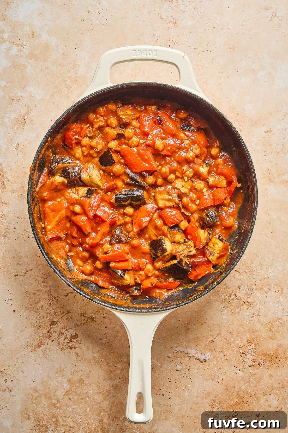 One-Pan Mediterranean Chickpea Skillet with Tomatoes & Spinach 18 A Mediterranean chickpea skillet brimming with eggplant and tomatoes simmers in a rich, red sauce against a beige surface.