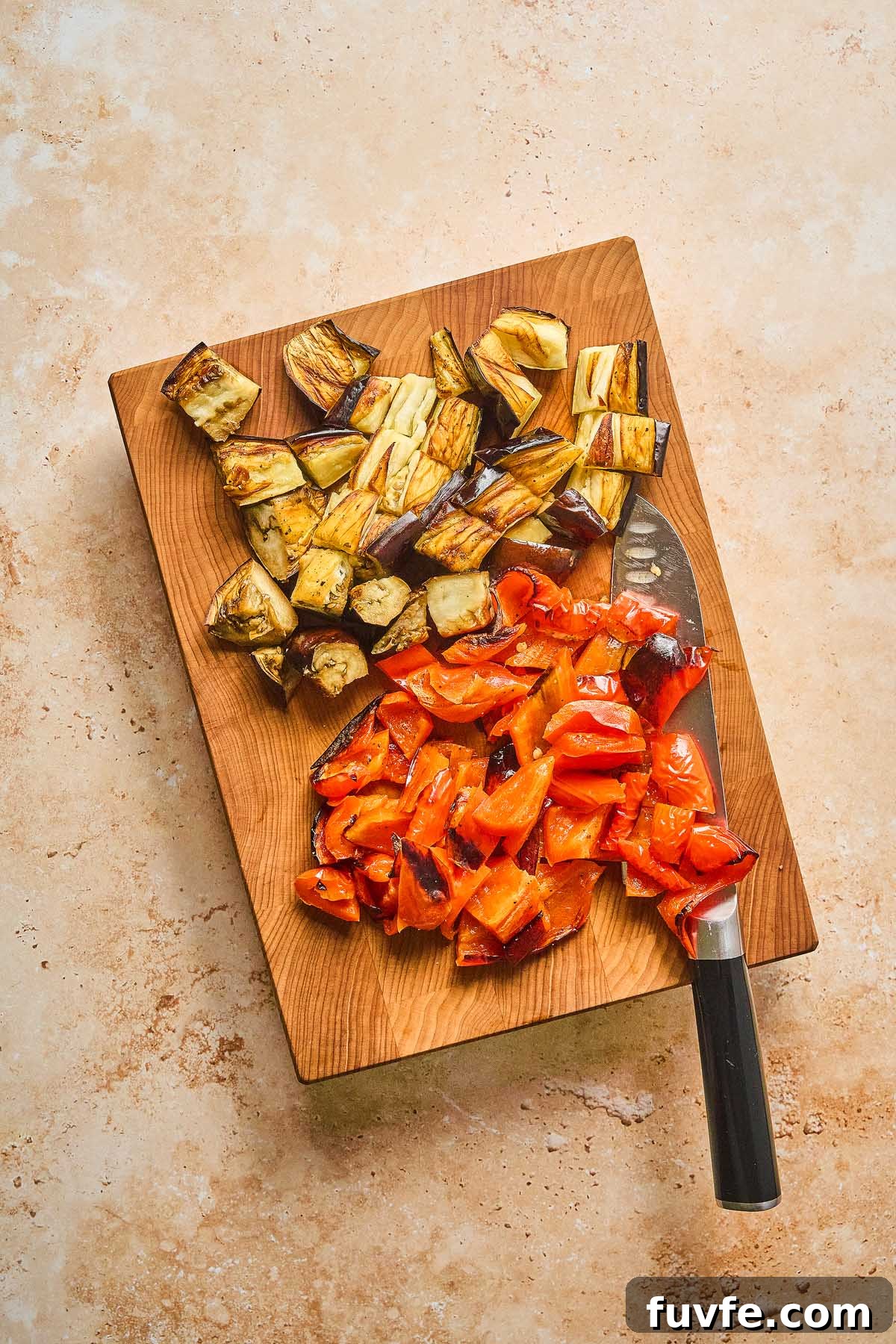 One-Pan Mediterranean Chickpea Skillet with Tomatoes & Spinach 19 Chopped roasted eggplant and red bell pepper rest on a wooden cutting board with a knife, ready to complement a Mediterranean chickpea skillet.