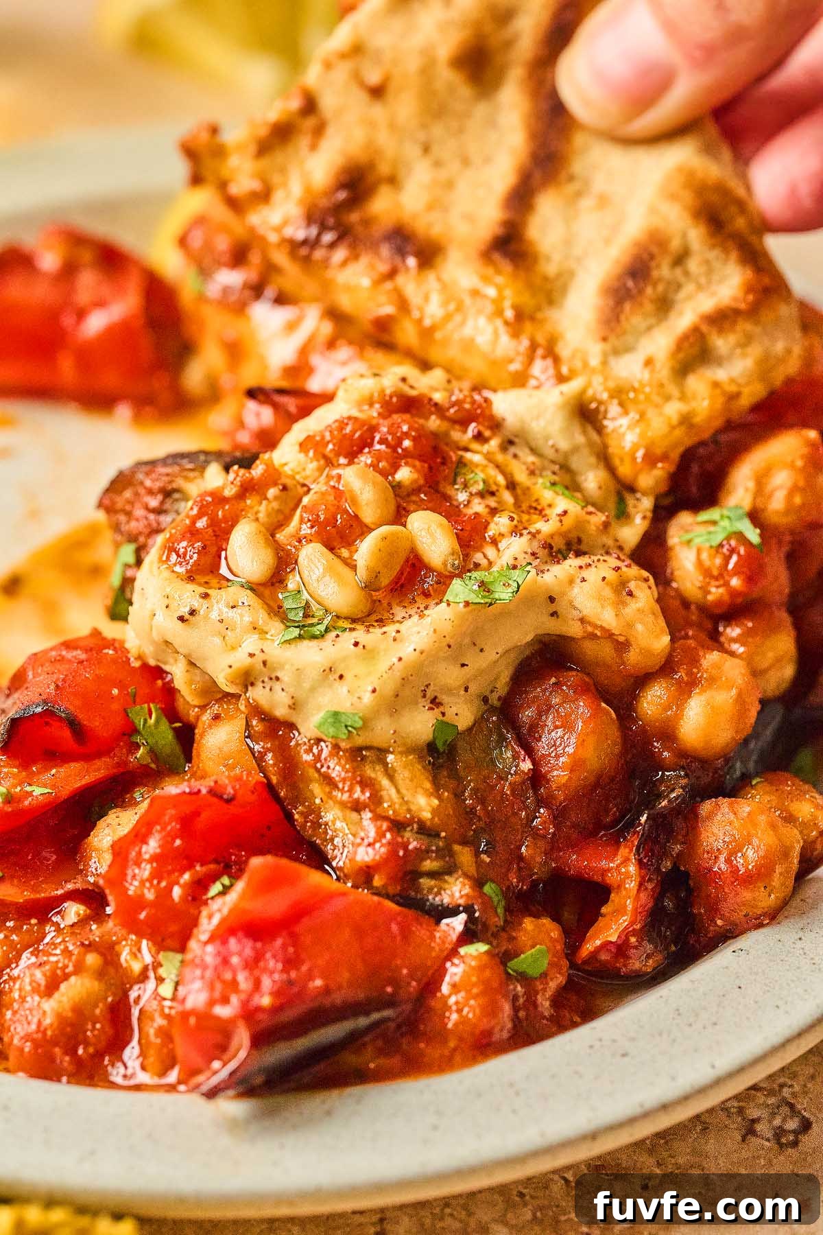 One-Pan Mediterranean Chickpea Skillet with Tomatoes & Spinach 4 A Mediterranean chickpea skillet delights with grilled vegetables and chickpeas topped with hummus and a sprinkle of pine nuts, while a hand reaches for a slice of pita bread.