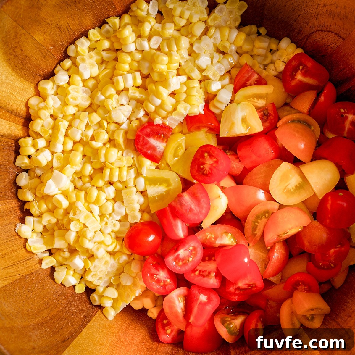 Fresh corn kernels and chopped cherry tomatoes in a wooden bowl.