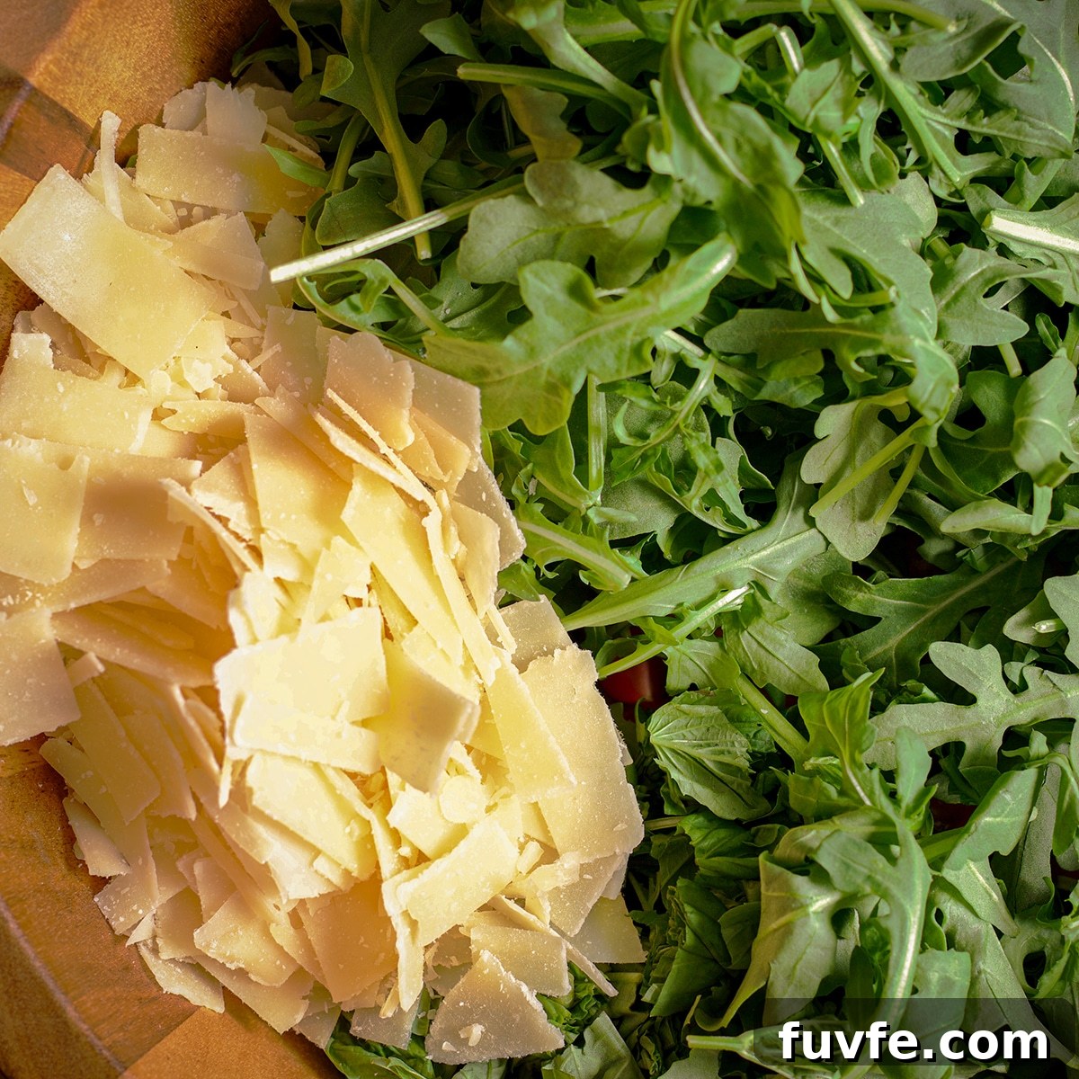 Shaved parmesan and arugula in a large wooden salad bowl.